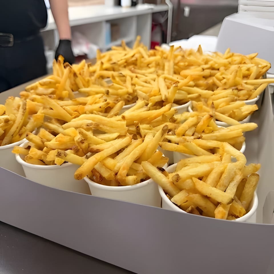 Many cups of golden french fries are arranged in a gray serving tray, with a person in the background.