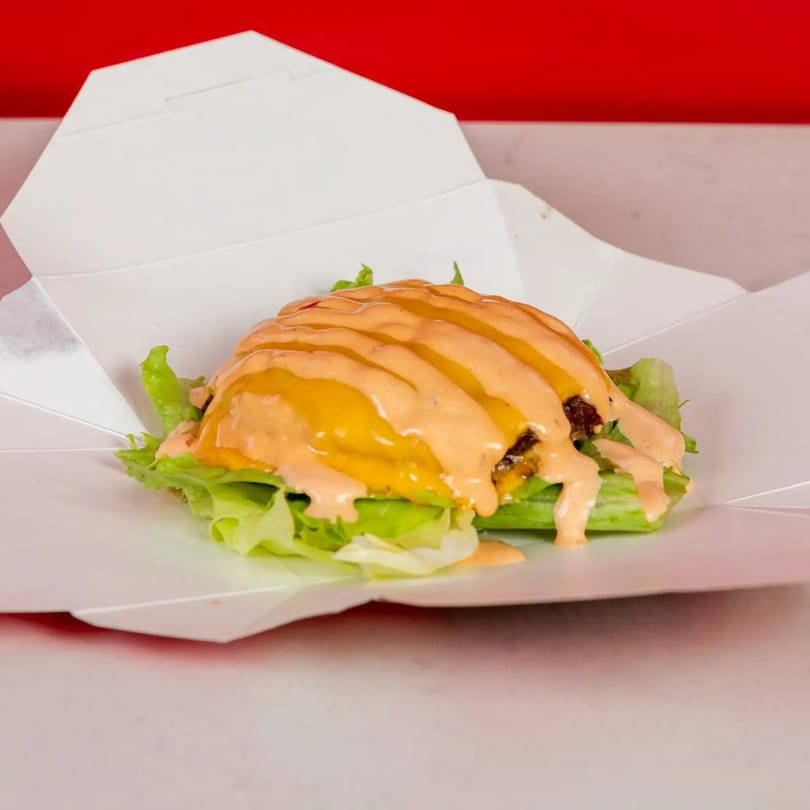 Lettuce-wrapped burger with melted cheese and special sauce in a white takeout container.
