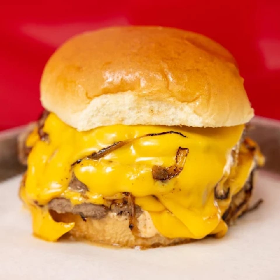 A Campus Burgers cheeseburger with melted yellow cheese and caramelized onions on a white bun.