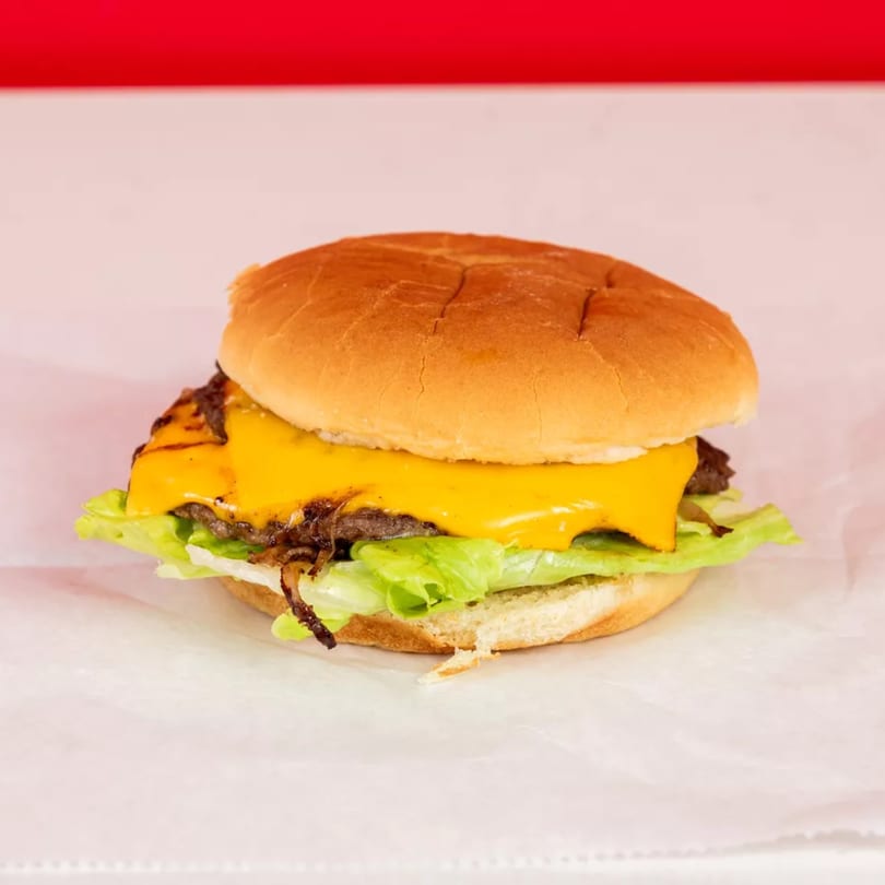 Cheeseburger with melted cheese, caramelized onions, and lettuce on a white bun, against a red and white background.