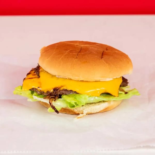 Cheeseburger with melted cheese, lettuce, and caramelized onions on a white bun.