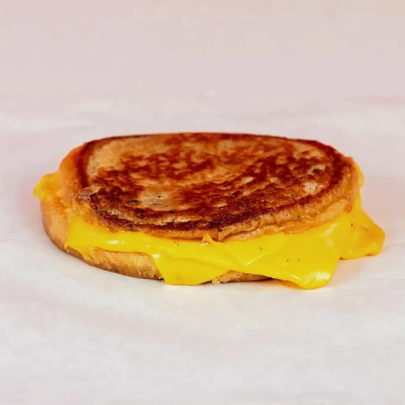 A golden-brown grilled cheese sandwich with melted yellow cheese oozing out, on a white surface.