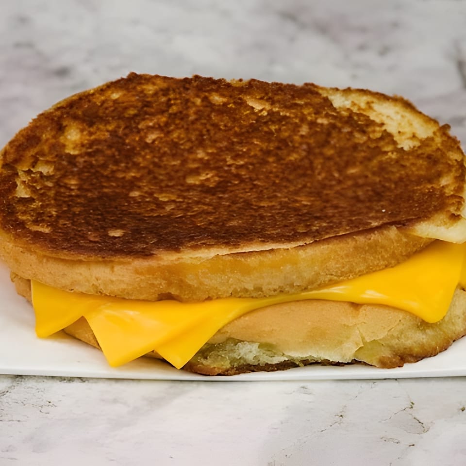 A golden-brown grilled cheese sandwich with melted yellow cheese on a white plate.