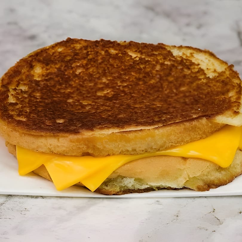 A golden-brown grilled cheese sandwich with melted yellow cheese on a white plate.