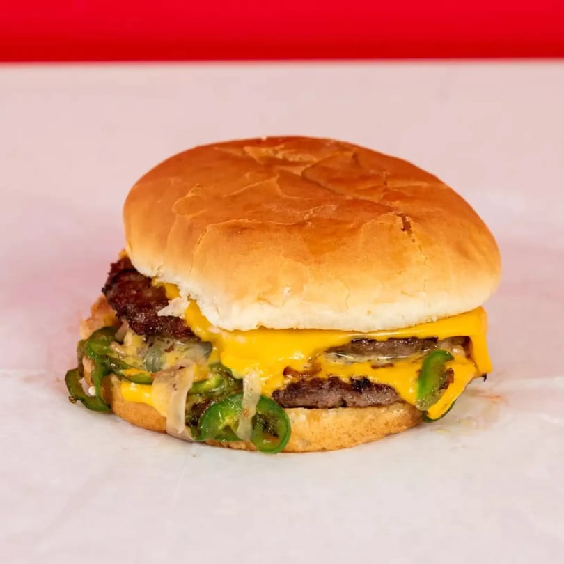 Double cheeseburger with melted cheese, grilled onions, and green peppers on a white bun.
