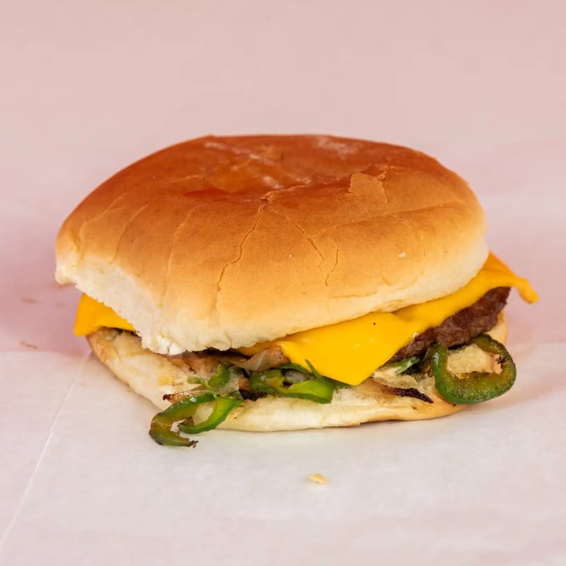 Cheeseburger with melted cheese, grilled onions, and sliced jalapeños on a bun.