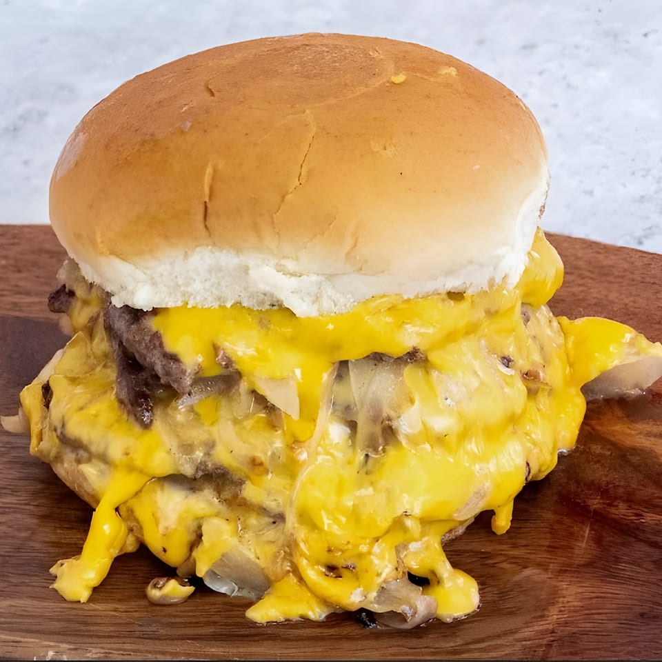 A double cheeseburger with melted yellow cheese and grilled onions on a wooden board.