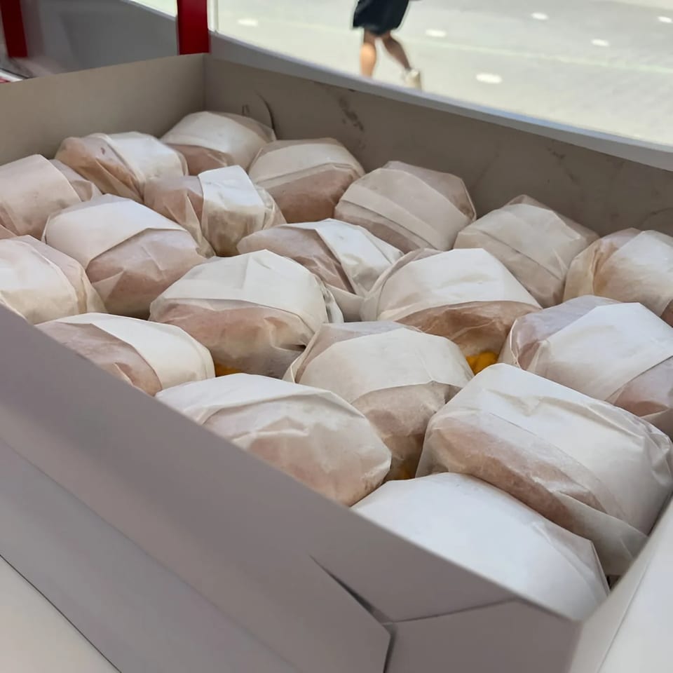 A white box filled with many Campus Burgers, each individually wrapped in paper.