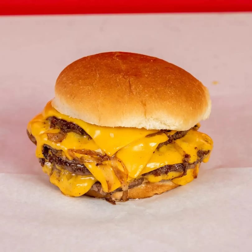 A double cheeseburger with melted cheese and caramelized onions on a white bun.