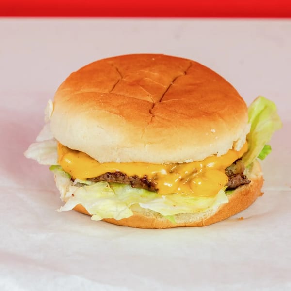 A cheeseburger with melted cheese, lettuce, and a bun, on white paper with a red background.