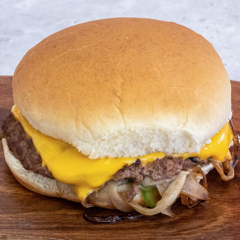 Campus Burgers' cheeseburger with melted cheese, grilled onions, and green peppers on a wooden board.