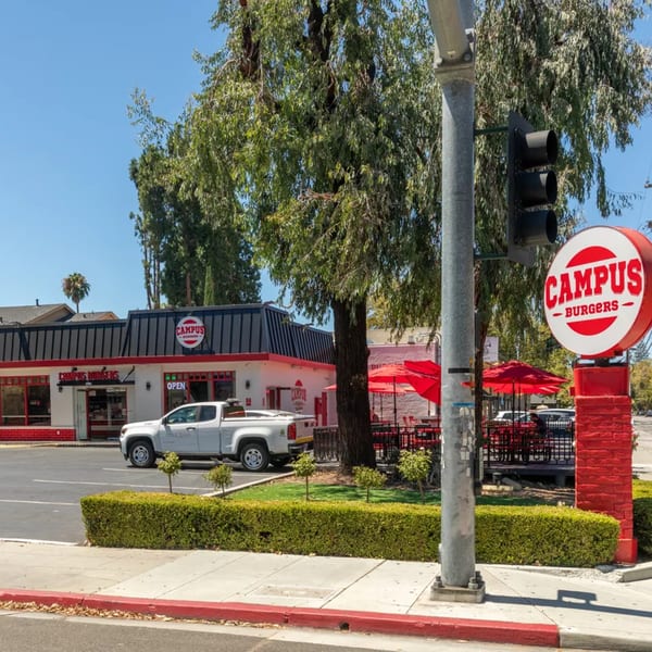 Campus Burgers restaurant exterior with a white truck, red umbrellas, and a large sign.
