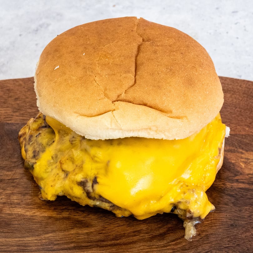 Campus Burgers' cheeseburger with melted yellow cheese oozing over the patty on a wooden board.