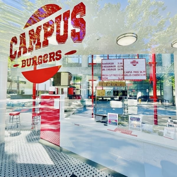 Reflective glass exterior of Campus Burgers, showing red signage, menu, and interior counter with stools.