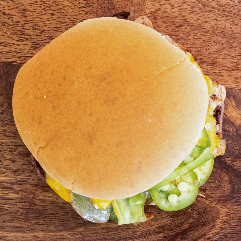 Top-down view of a Campus Burgers cheeseburger with lettuce and jalapeños on a wooden surface.