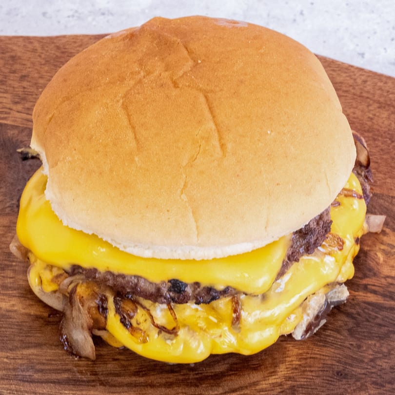 Campus Burgers' cheeseburger with melted cheese and caramelized onions on a wooden board.