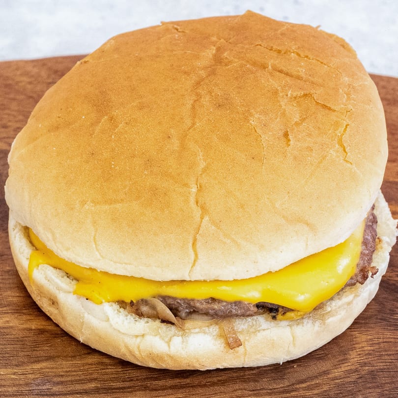 Campus Burgers' cheeseburger with melted yellow cheese and caramelized onions on a wooden board.