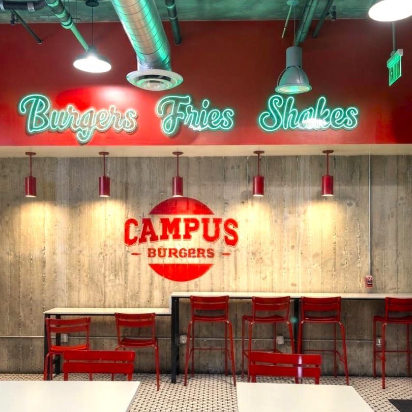 Campus Burgers restaurant interior with red walls, neon signs, concrete wall, and red bar stools.