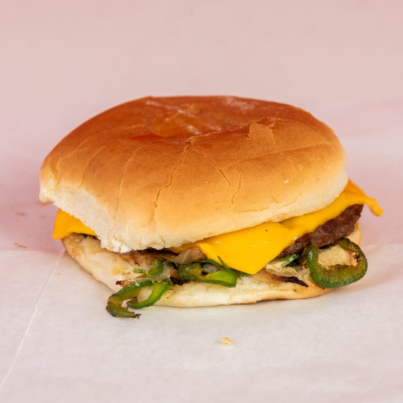 Cheeseburger with melted cheese, grilled onions, and sliced jalapeños on a bun.