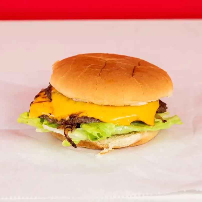 Cheeseburger with melted cheese, lettuce, and caramelized onions on a white bun.
