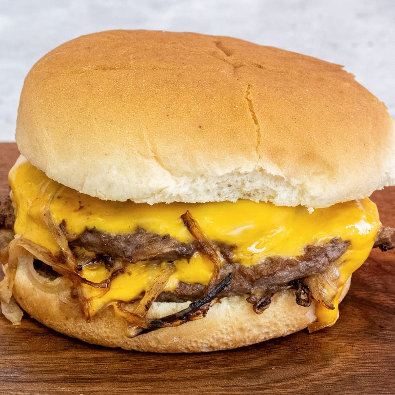 Campus Burgers' double cheeseburger with melted cheese and caramelized onions on a wooden surface.