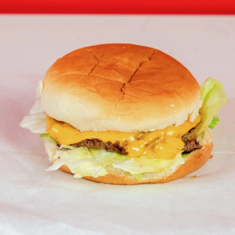 Cheeseburger with melted cheese, lettuce, and a beef patty on a bun, on white paper.
